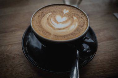 Bir kafede ahşap bir kırsal masanın üstünde kapuçino içeceği oturuyordu.