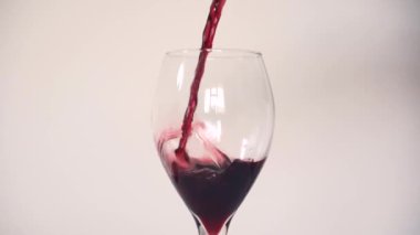 Kırmızı şarabı boş bir gözyaşı damlasına dökerek şarap kadehini düz beyaz arka plana yavaşça dökerek.