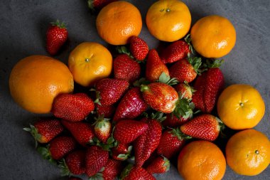Koyu gri arka planda bir sürü taze portakal ve çilek. Organik meyveli fotoğraf. Sulu yaz meyvelerinin renkli bir resmi. Boşluğu kopyala. 