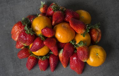 Koyu gri arka planda bir sürü taze portakal ve çilek. Organik meyveli fotoğraf. Sulu yaz meyvelerinin renkli bir resmi. Boşluğu kopyala. 