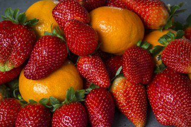 Koyu gri arka planda bir sürü taze portakal ve çilek. Organik meyveli fotoğraf. Sulu yaz meyvelerinin renkli bir resmi. Boşluğu kopyala. 