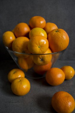 Cam kasede bir sürü portakal var. Yaz meyveleri hala hayattadır. Koyu gri arkaplan. 