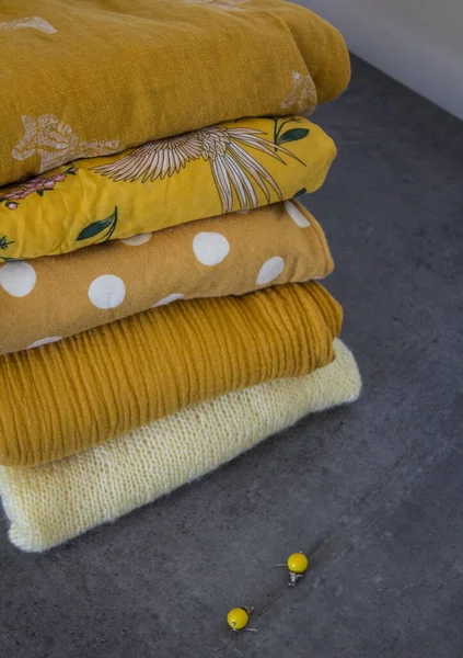 Stack of clean freshly laundered, neatly folded women\'s clothes. Fabric of different types. Cotton fabric texture. Copy space, close up, top view. A lot of yellow dresses with different prints.