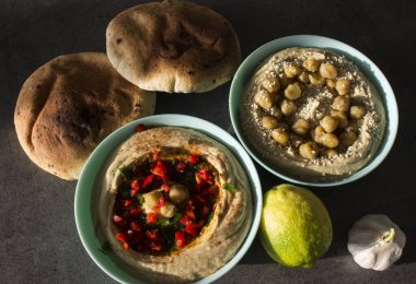 Koyu gri masada iki farklı humus türü var. Masada pita ekmeği olan taze ev yapımı humus tabağı. Ortadoğu 'nun otantik yemekleri. Sağlıklı beslenme konsepti. Vejetaryen dengeli yemek. İsrail 'in geleneksel yemeği. 