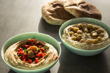Koyu gri masada iki farklı humus türü var. Masada pita ekmeği olan taze ev yapımı humus tabağı. Ortadoğu 'nun otantik yemekleri. Sağlıklı beslenme konsepti. Vejetaryen dengeli yemek. İsrail 'in geleneksel yemeği. 