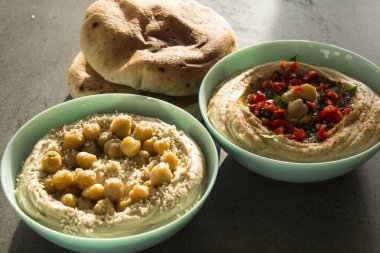 Koyu gri masada iki farklı humus türü var. Masada pita ekmeği olan taze ev yapımı humus tabağı. Ortadoğu 'nun otantik yemekleri. Sağlıklı beslenme konsepti. Vejetaryen dengeli yemek. İsrail 'in geleneksel yemeği. 