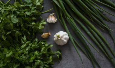 İçindekiler üst görünüm. Masada taze sebzeler var. Koyu gri arka plan. Kopya uzayı ile basit kompozisyon. Yeşil soğan, sarımsak, domates, maydanoz. 