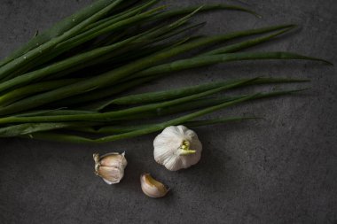 İçindekiler üst görünüm. Masada taze sebzeler var. Koyu gri arka plan. Kopya uzayı ile basit kompozisyon. Yeşil soğan, sarımsak, domates, maydanoz. 