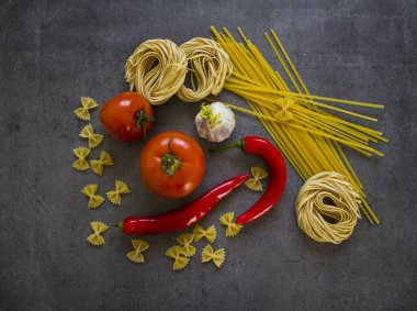 Farklı türde makarna ve taş masada taze sebzelerle güzel bir hayat. Koyu gri arka planda İtalyan yemek malzemeleri. Bölgesel yiyecekler yakın çekim fotoğrafı. Canlı renkler.
