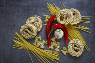 Farklı türde makarna ve taş masada taze sebzelerle güzel bir hayat. Koyu gri arka planda İtalyan yemek malzemeleri. Bölgesel yiyecekler yakın çekim fotoğrafı. Canlı renkler.