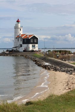 Kırmızı çatılı beyaz deniz feneri. Yaz deniz manzarası. Bulutlu güzel suluboya gökyüzü. Klasik Hollandalı mimarisi. Hollanda 'da Yaz.  