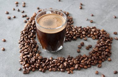 Günaydın! Günaydın! Şeffaf kahve fincanı, masada kavrulmuş fasulye. Fotokopi alanı olan gri arkaplan. Kahve çekirdeğinden yapılmış bir kalp.. 