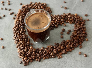 Günaydın! Günaydın! Şeffaf kahve fincanı, masada kavrulmuş fasulye. Fotokopi alanı olan gri arkaplan. Kahve çekirdeğinden yapılmış bir kalp.. 