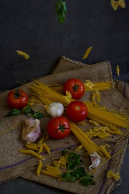 Uçan makarna. Domateslerle ve farklı türde makarnalarla dolu bir hayat. Taze malzemeler kapanıyor. Koyu gri arka plan. Geleneksel yemek. Yiyecek havada asılı fotoğrafı.. 