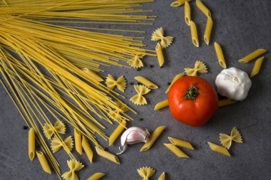 Domateslerle ve farklı türde makarnalarla dolu bir hayat. Taze malzemeler üst görünümde. Koyu gri arka plan. Geleneksel yemek.. 