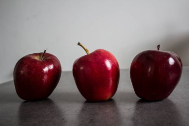 Taş masada üç kırmızı sulu elma. Fotokopi alanı olan koyu gri bir arkaplan. Basit bir kompozisyon. Meyveli natürmort. İçindekiler üst görünüm. 