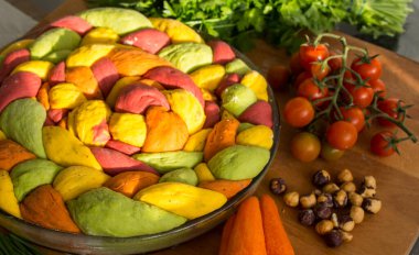 Ahşap masanın üzerinde pişirme formundaki renkli challah ekmeği. Taze sebzeler. Üst görünüm fotoğrafını içerir.