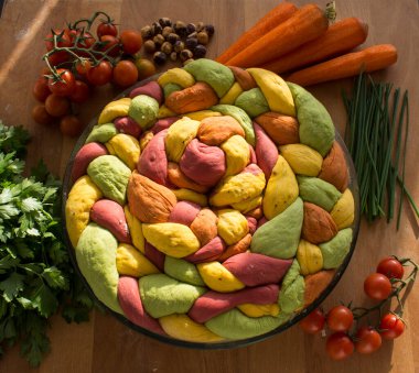 Ahşap masanın üzerinde pişirme formundaki renkli challah ekmeği. Taze sebzeler. Üst görünüm fotoğrafını içerir.