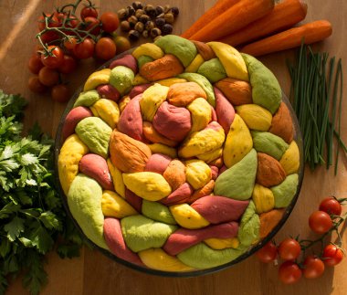 Ahşap masanın üzerinde pişirme formundaki renkli challah ekmeği. Taze sebzeler. Üst görünüm fotoğrafını içerir.
