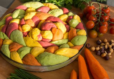 Ahşap masanın üzerinde pişirme formundaki renkli challah ekmeği. Taze sebzeler. Üst görünüm fotoğrafını içerir.