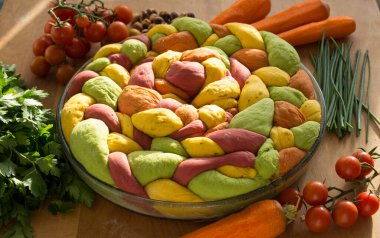 Ahşap masanın üzerinde pişirme formundaki renkli challah ekmeği. Taze sebzeler. Üst görünüm fotoğrafını içerir.