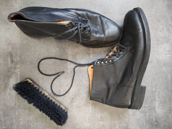 Pair of black leather retro shoes and wooden shoe brush on grey background with copy space.