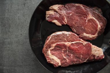 Çiğ et dokusu. Siyah ızgarada biftek. Kopyalama alanı olan gri arkaplan.