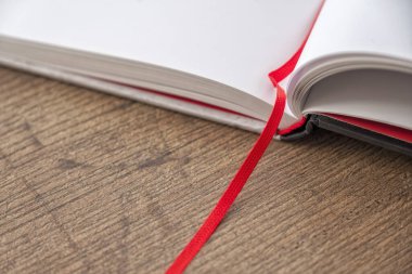 Boş sayfalarla açılan defter. Sert kaplamalı karton kapak, açık kitap, temiz beyaz sayfalar, kırmızı kumaş yer imi. Yumuşak gölgeler ve doğal ışık onu kar beyazı bir yüzey gibi gösteriyor..