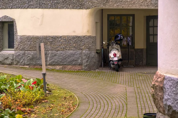 Park etmiş scooterlı, şık ve zarif bir avlusu var. Eski bir duvar evi. Düzgün asfalt bir yol..