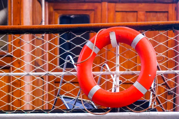 Parlak turuncu şişirilebilir cankurtaran / cankurtaran metal ızgaralı ahşap korkulukta asılı. Boğulmayı önle. Ahşap arkaplan. 