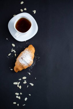 Beyaz kahve fincanı, siyah arka planda kruvasan. Kahvaltı konsepti