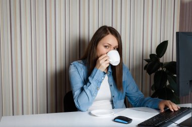 Elinde bir fincan kahve olan genç bir kadın iş yerinde notlar alıyor. Evde kal. Kız beyaz bir masadaki deftere fikirler yazıyor..