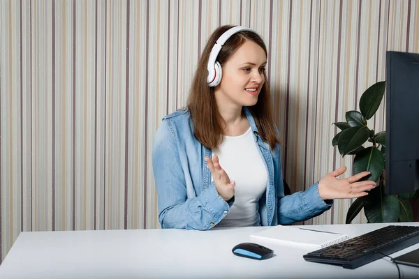 Young woman communicates via webcam. Head shot close up portrait happy pleasant young woman looking at camera. Stay at home. Isolated young woman in blue casual jeans shirt in headphones on head.