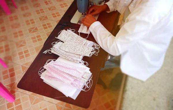 A tailor with a sewing machine, a white shirt on a Sunday morning, a small floral pattern, a spread-resistant mask on a wooden table, copying the area. Asian handmade work