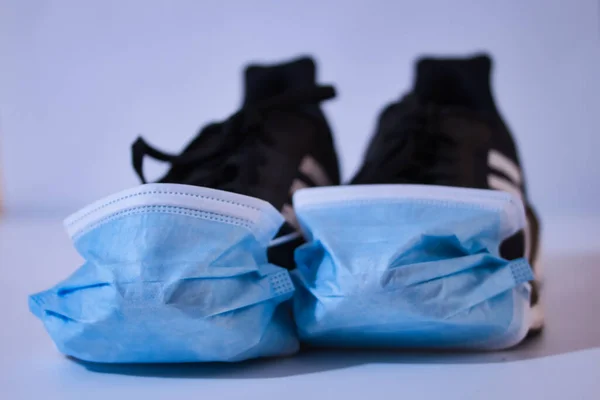 Running shoes with mask during Covid 19 pandemic. Black shoes with blue mask. White background and out of focus.