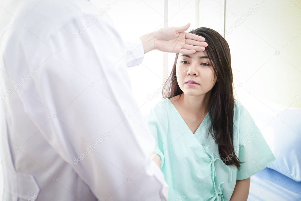 An Asian male doctor uses the back of her hand to hold the forehead of a female patient. To check the body heat temperature. The concept of health examination and medical services in hospitals