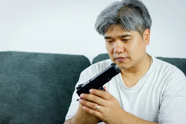 Older men have stress, have business problems and live life. Sitting holding the gun on the sofa thinking of shooting himself. Concept of violence