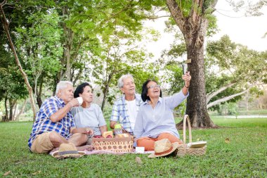 Bir grup Asyalı son sınıf öğrencisi gölgeli bahçede oturup, rahatlayıp yemek hazırlıyorlar. Mutlular ve birlikte fotoğraf çekmek için cep telefonu kullanıyorlar. Yaşlılar topluluğunun kavramları. Parkta piknik.