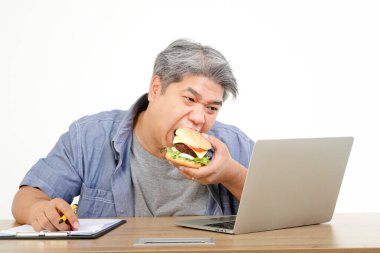 Hamburger yiyen şişman yaşlı bir adam işe oturuyor. Yaşlılar için sağlıklı beslenme kavramı. Beyaz arkaplan