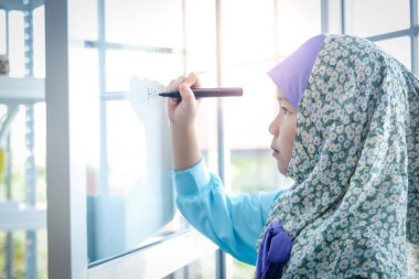 İslamcı kızlar okulda okuyor ve tahtaya numaralar yazıyor. Asya 'daki çocukların eğitimsel gelişim kavramı