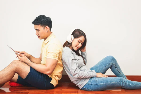 Asian couples sit back against each other, listen to music, and play the tablet. Happy to live together in his own home. Modern family concept