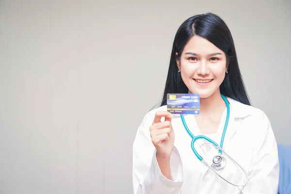 美しいアジアの医師は 明るい白の背景に笑みを浮かべて立ってクレジットカードを保持 医療サービスの概念と1枚のカードで金融 — ストック写真