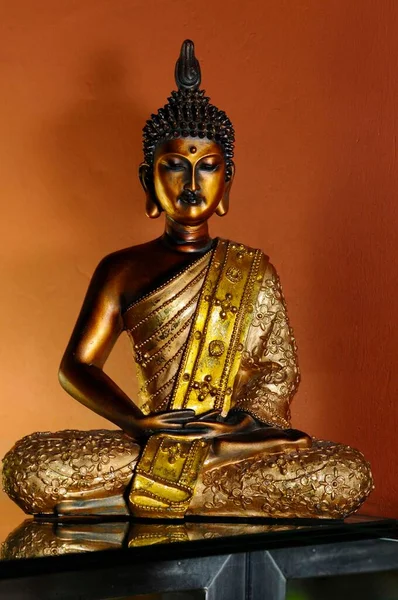 Złoty Posąg Buddy Czarnym Stole Pomarańczowe Tło — Zdjęcie stockowe