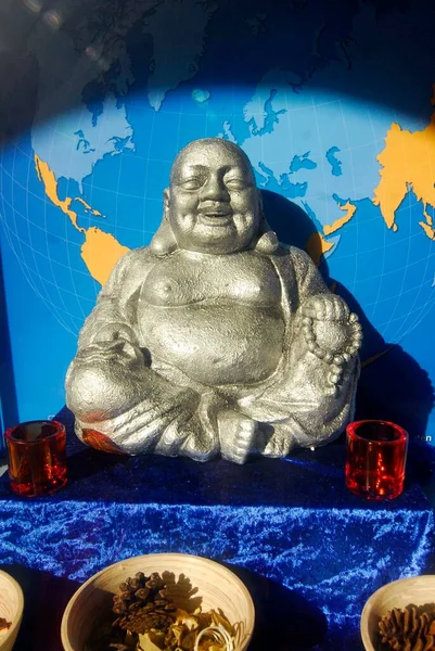 statue of laughing Buddha in front of blue world map