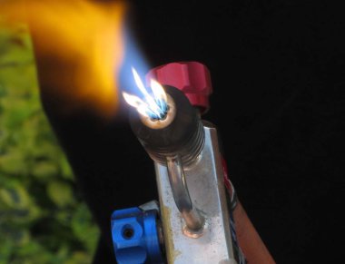 Gaz ocağı, turuncu ve mavi alevle ateş yakıyor.