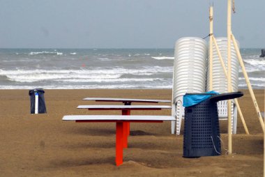 Gri bir günde kumsal, sandalyeli dalgalar ve çöp tenekeleri