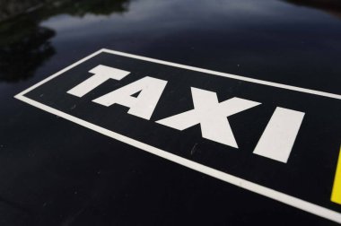 Bir arabanın kaputunda siyah beyaz bir taksi tabelası var.