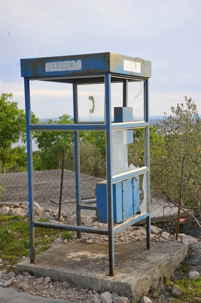 Abandoned and broken public telephone booth with broken glass and rusty metal