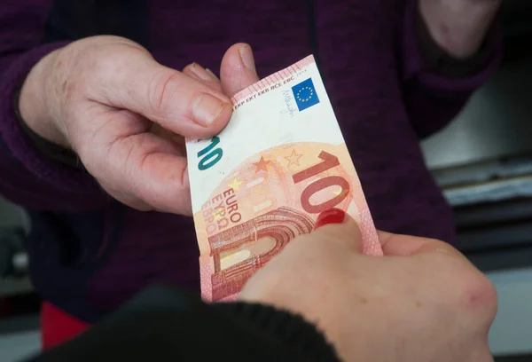 person giving money to another person, cash transaction with a ten euro banknote