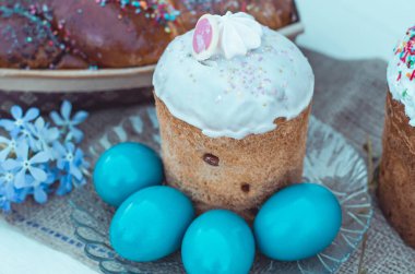 Paskalya pastası kompozisyonu. Şeffaf plakalı bir Paskalya. Maviyle boyanmış Paskalya yumurtaları. Paskalya, yumurta ve çiçekler çuval bezinde yatıyor.